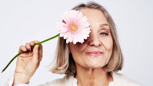 Mulher aposentada sorrindo com flor no rosto, representando leveza e bem-estar na terceira idade